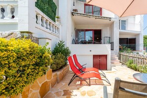 Un edificio de dos plantas con fachada de piedra, un balcón con mobiliario exterior y una escalera que conduce al nivel superior.