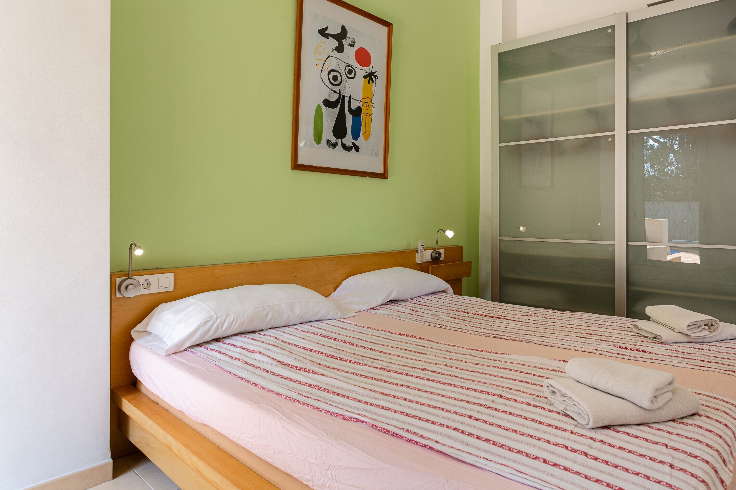 Una cama con colcha a rayas, cabecera y una obra de arte colgada en la pared.