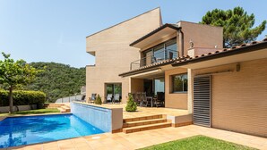 A modern house with a swimming pool, outdoor seating, and a view of the hills. - Exclusive Villa with Pool, Sea View, and Wi-Fi (Tossa De Mar)