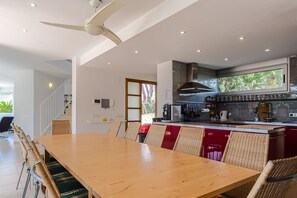 Une cuisine moderne dotée d’un grand îlot central, d’un coin repas avec une table en bois et des chaises en osier, et d’un ventilateur de plafond.