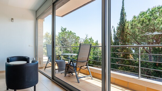 A balcony with a chair, a table, and a view of trees and buildings. - Exclusive Villa with Pool, Sea View, and Wi-Fi (Tossa De Mar)