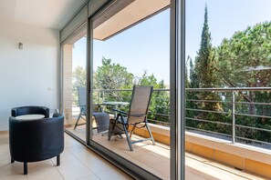 Un balcon avec une chaise, une table et une vue sur les arbres et les bâtiments.