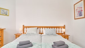 A double bed with a wooden headboard, two bedside tables with lamps, a nightstand, and a wall-mounted painting.