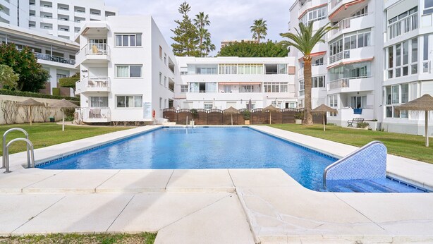 A swimming pool with a clear blue water surface, surrounded by a paved deck.