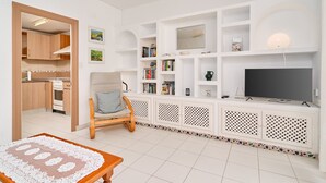 A living room with a TV, bookshelves, a chair, and a kitchen area.