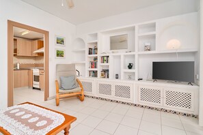A living room with a TV, bookshelves, a chair, and a kitchen area.
