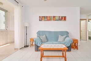 A living room with a sofa, a coffee table, a lamp, and a wall art piece. - Large 1-bed Apartment with Shared Pool, Garden, A/C & Wi-Fi (Nerja)
