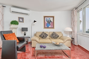 A living room with a sofa, armchair, coffee table, and a painting on the wall.