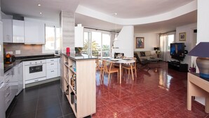 Una cocina moderna con armarios blancos, un comedor con mesa y sillas redondas, y una sala de estar con sofá y televisor.