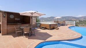 A rooftop pool area with a bar, seating, and a view of the hills.