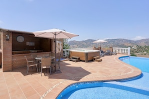 A rooftop pool area with a bar, seating, and a view of the hills.