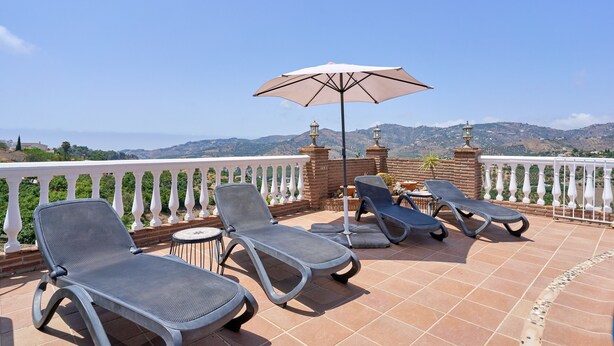 A terrace with lounge chairs and a table, overlooking a scenic landscape.