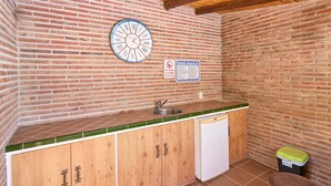 A small kitchenette with a brick wall, a clock, a sink, and a trash bin.