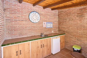 A small kitchenette with a brick wall, a clock, a sink, and a trash bin.
