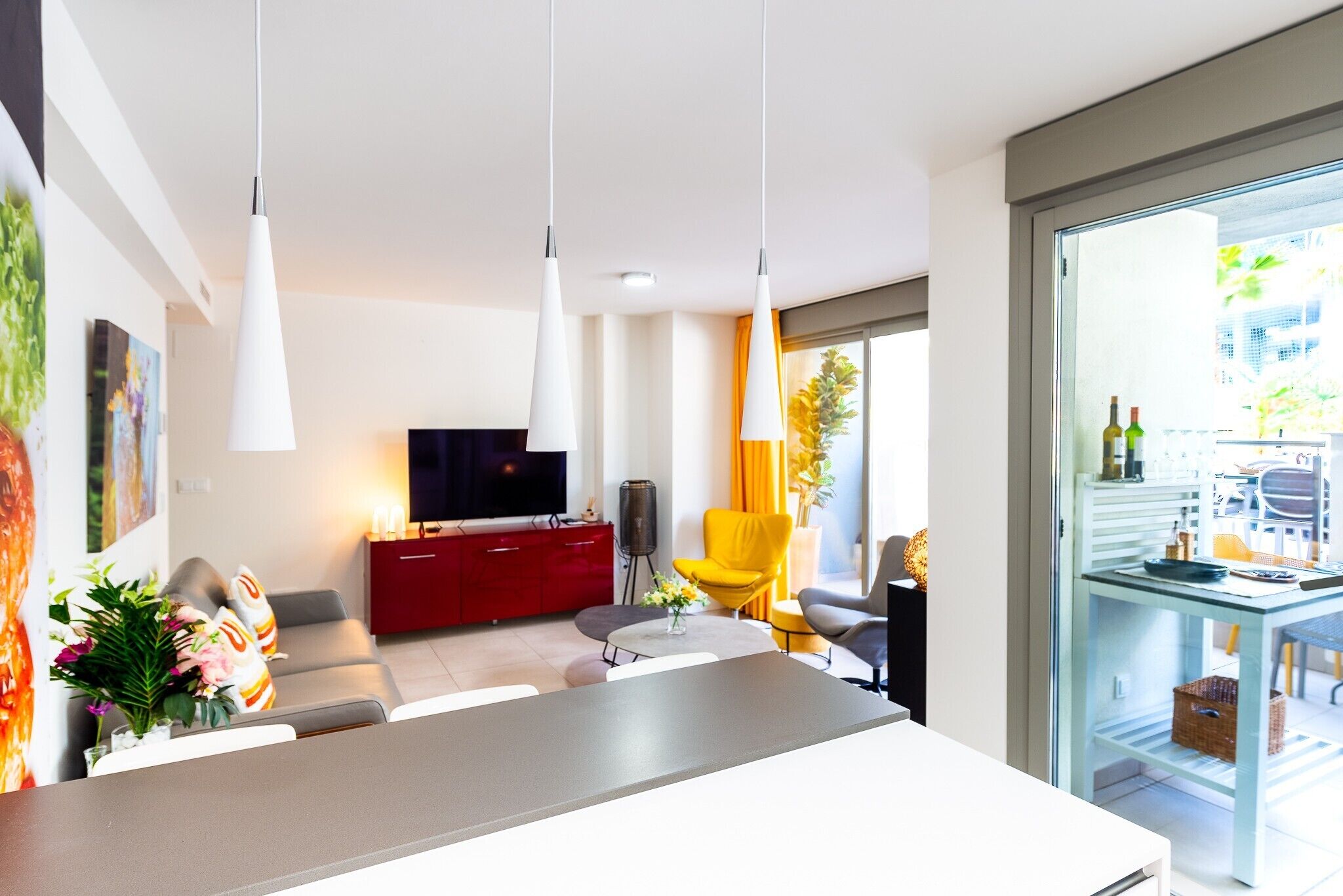 Una sala de estar moderna con un televisor de pantalla plana, un mueble rojo, un sillón amarillo y una mesa de comedor de vidrio.