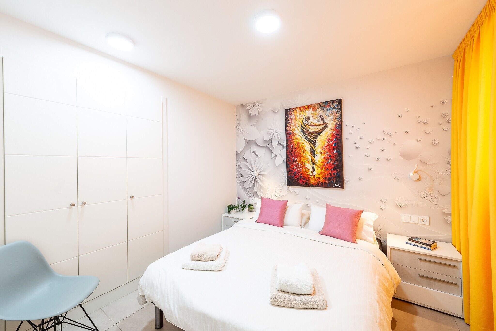 Een moderne slaapkamer met een bed, nachtkastjes, een stoel en een schilderij aan de muur.