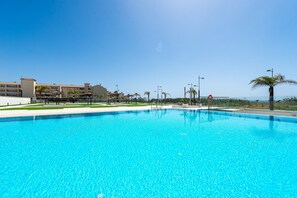 Una piscina blava i cristal·lina amb una cadira de socorrista i una palmera al fons.