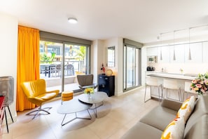 A modern living room with a sofa, a yellow chair, a coffee table, and a balcony with outdoor seating.
