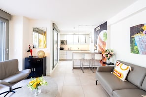 A modern living room with a sofa, a coffee table with flowers, and a dining area with chairs and a kitchen in the background. - Apartment 'Luxurious Two Bed' with Private Terrace, Wi-Fi and Air Conditioning (Torrox)
