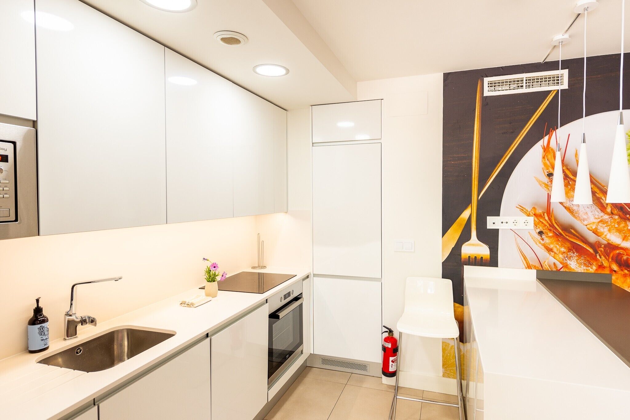 A modern kitchen with stainless steel appliances, a sink, and a fire extinguisher.