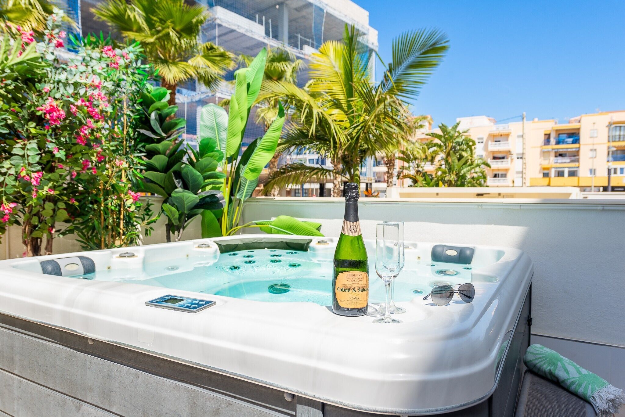 Een jacuzzi met een champagnefles en een glas, omgeven door weelderige begroeiing en een heldere lucht.