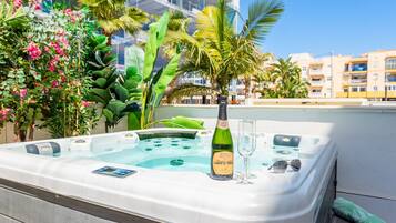 Een jacuzzi met een champagnefles en een glas, omgeven door weelderige begroeiing en een heldere lucht.