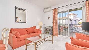 Ein Wohnzimmer mit Sofa, Couchtisch, Fernseher und einem Balkon mit Blick auf Gebäude.