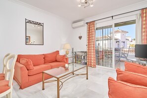 Un salon comprenant un canapé, une table basse, un téléviseur et un balcon offrant une vue sur les immeubles.