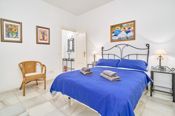 A bedroom with a bed, two bedside tables, a chair, and artwork on the walls.