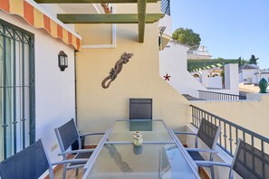 A balcony with a glass table, chairs, and a decorative metal piece.