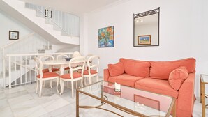 Una sala de estar con una escalera, una mesa de centro de vidrio, un sofá y dos cuadros en la pared.
