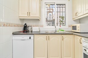 Une cuisine avec des meubles blancs, un lave-vaisselle Bosch, un four à micro-ondes et une fenêtre donnant sur un immeuble.