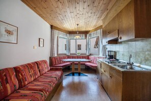 Una stanza accogliente con soffitto in legno, un tavolo da pranzo con panche, un angolo cottura e un divano.