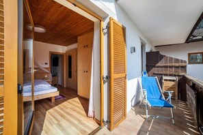 Een slaapkamer met een houten plafond, een bed en een schuifdeur naar een balkon met een blauwe stoel en een houten tafel.