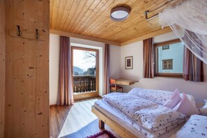 Una camera da letto con soffitto in legno, un letto con biancheria da letto floreale, una scrivania e una finestra con tende.