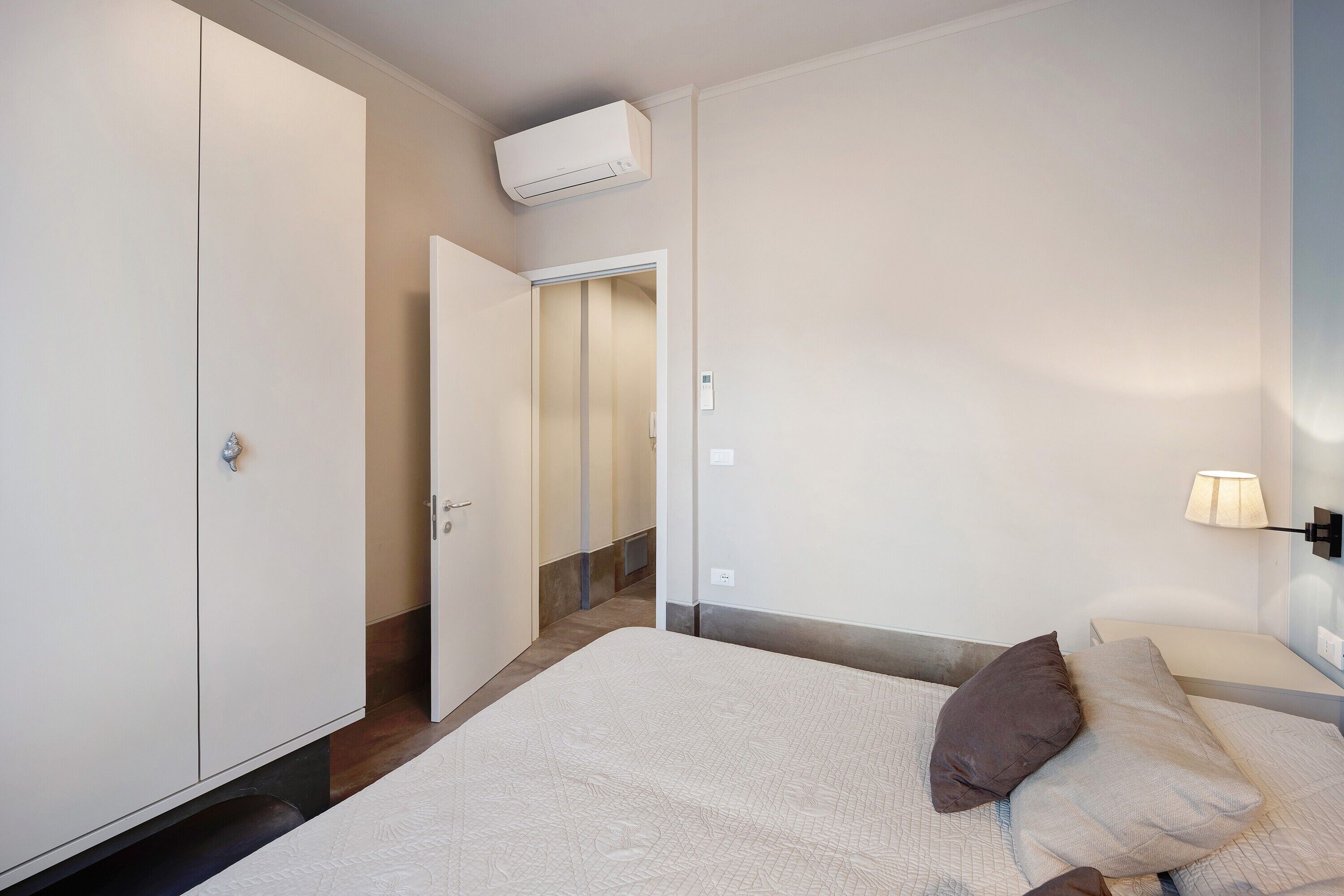 Een slaapkamer met een bed, nachtkastje, lamp, kledingkast en een airconditioning.