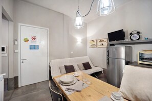Un espace de vie compact comprenant un coin cuisine, un coin repas avec une table dressée pour deux personnes et un lit avec des oreillers.