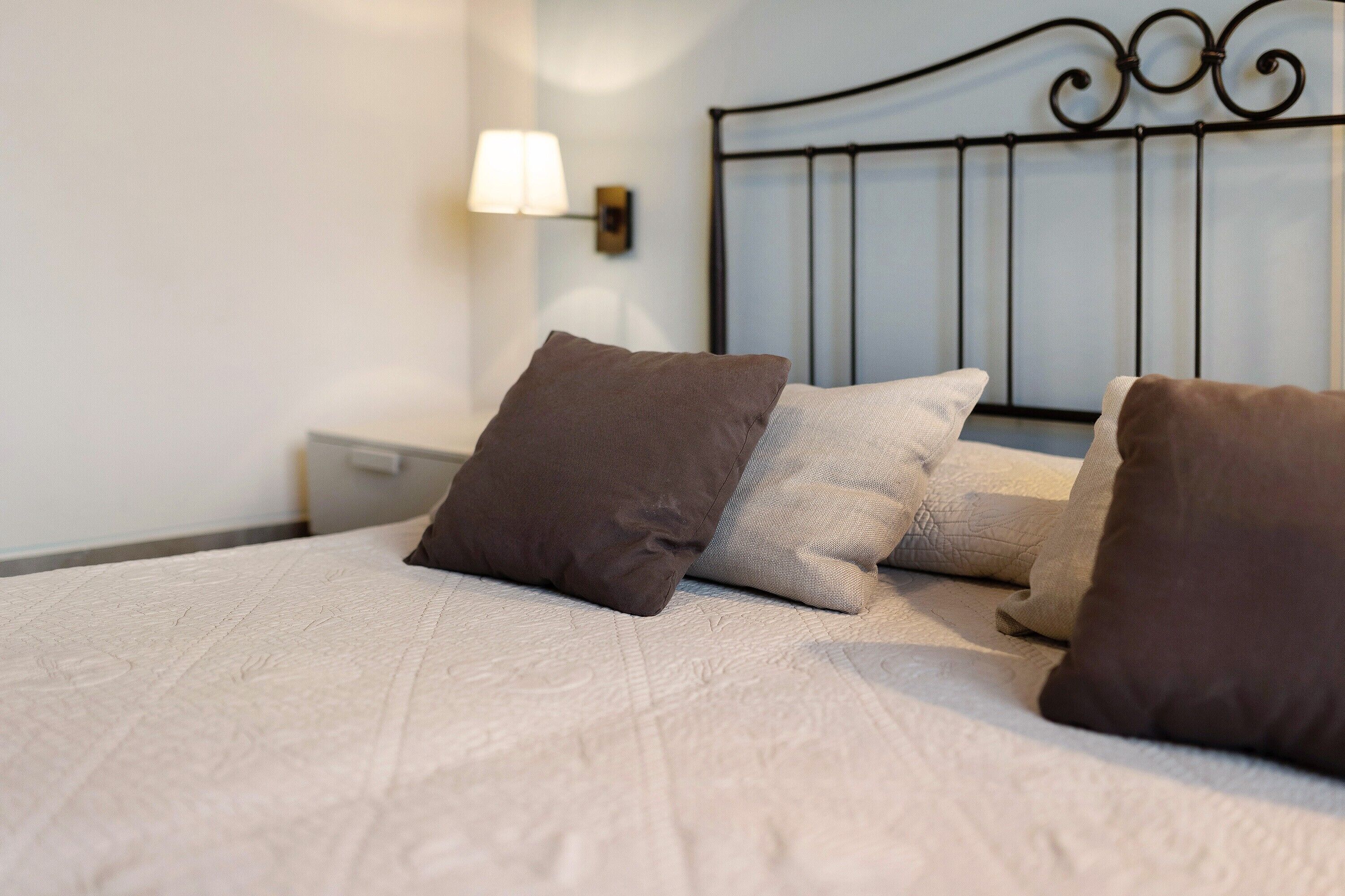 A bed with a textured white cover, a metal headboard, and two pillows.
