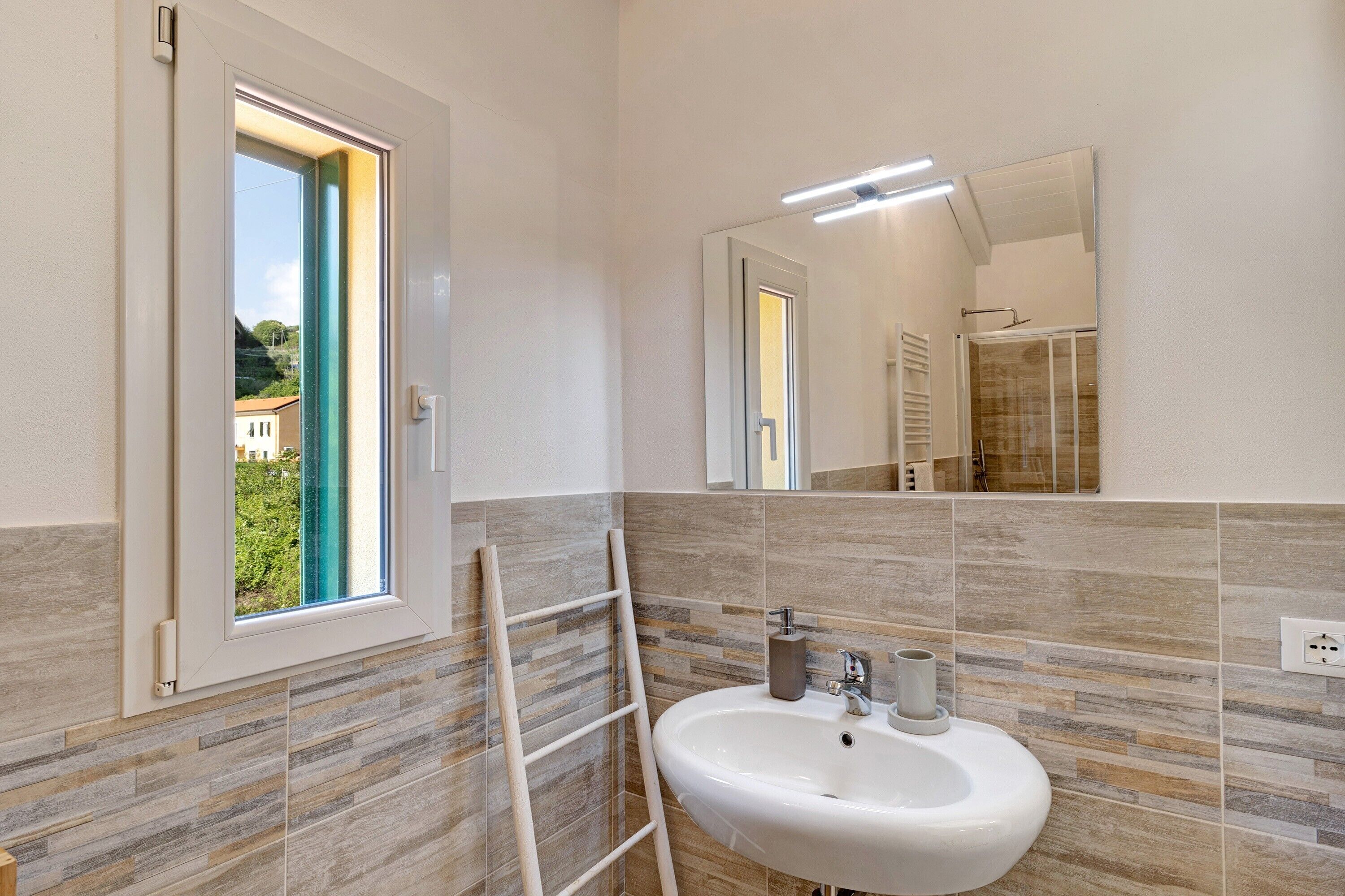 A bathroom with a window, a sink, a mirror, and a shower area.