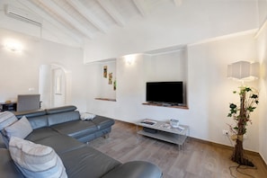 A modern living room with a grey sectional sofa, a flat-screen TV mounted on the wall, a small side table, and a decorative plant.