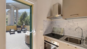 A kitchen with a sink, stove, and cabinets, and a patio with chairs and a grill. - Ca di Perti Apartment 3 with Mountain View (Finale Ligure)