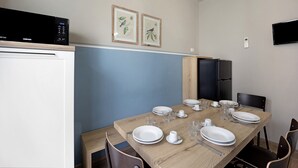 Ein Essbereich mit einem Holztisch, gedeckt für vier Personen, einer schwarzen Mikrowelle und zwei gerahmten botanischen Drucken an der Wand.