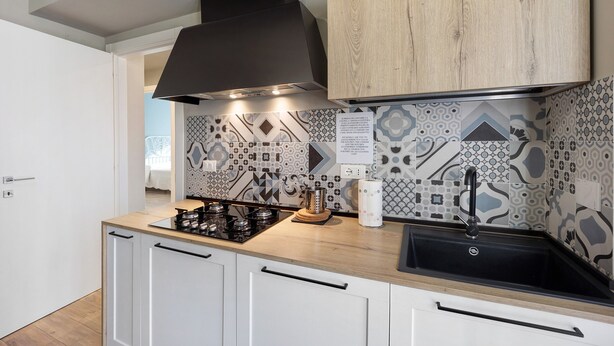 Eine moderne Küche mit Gasherd, schwarzem Dunstabzug, weißen Schränken und einem backsplash mit gemusterten Fliesen.