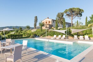 A pool area with lounge chairs and umbrellas, a stone building in the background, and a clear sky. - Belvilla by OYO Pergola (Vinci)