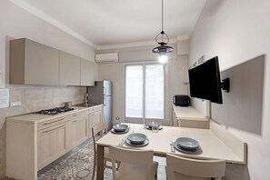 A modern kitchen with a dining table set for two, a built-in stove, and a flat-screen TV mounted on the wall.