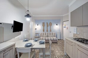 A compact kitchen with a dining table, chairs, a sofa, and a TV mounted on the wall.