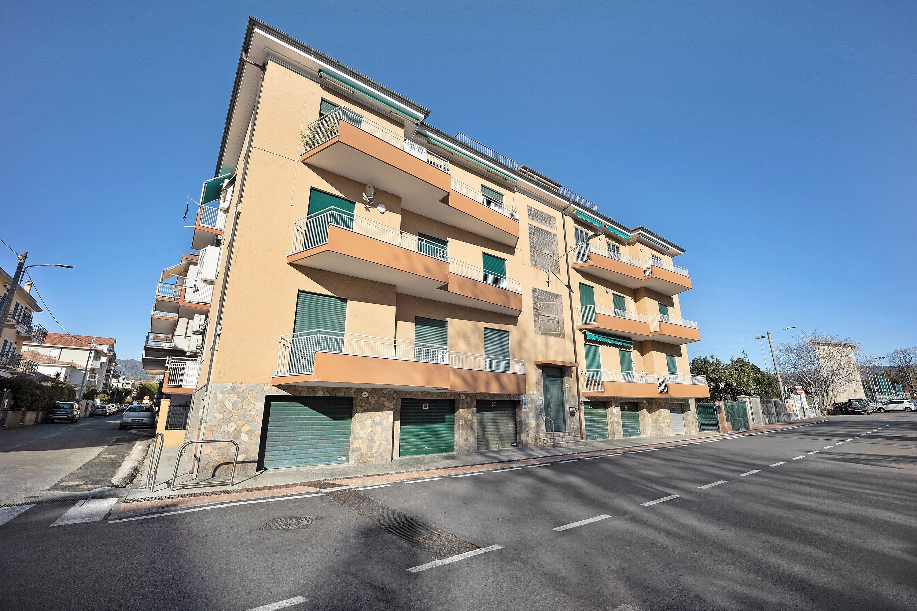 Un immeuble résidentiel à plusieurs étages, doté de balcons, d’un garage et surplombant un ciel dégagé.