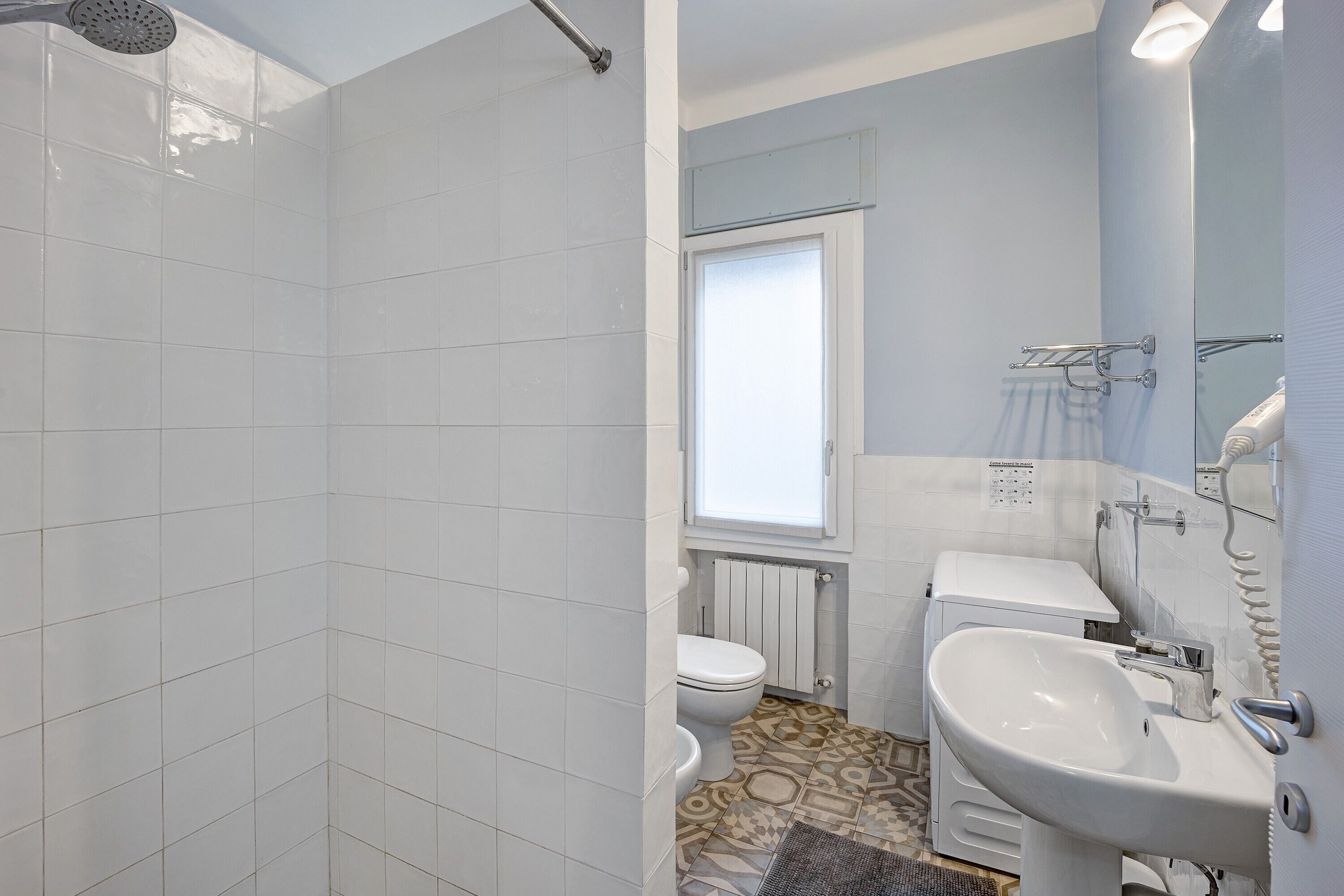 Une salle de bain avec des carreaux blancs, des toilettes, un lavabo et une douche.
