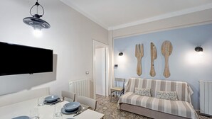 Un salon moderne avec un canapé, une table à manger dressée avec des assiettes et des couverts, un téléviseur à écran plat et des ustensiles de cuisine en bois fixés au mur.