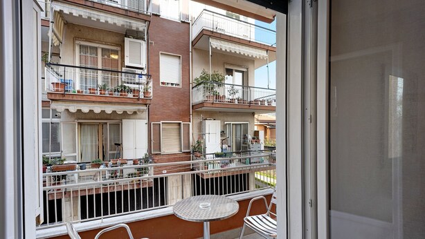 Un balcon avec une table et des chaises, une vue sur les bâtiments voisins et une porte donnant sur l’intérieur.